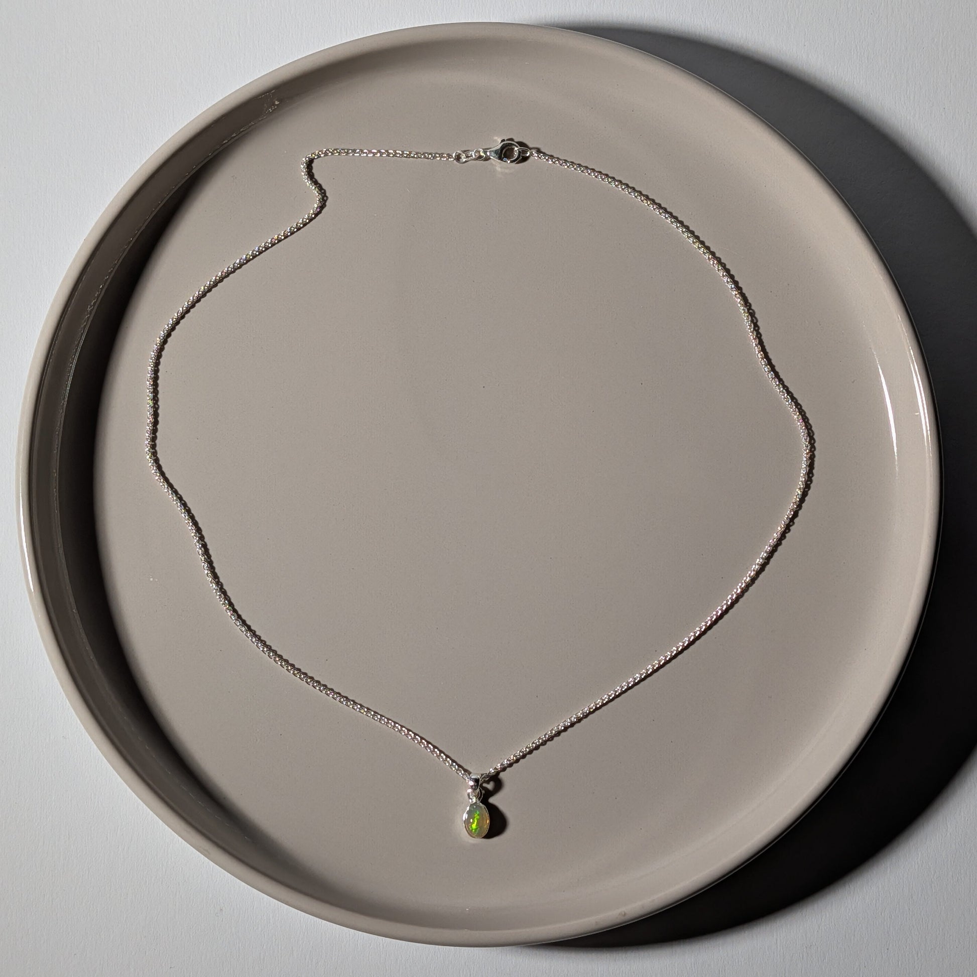 Polierter ovaler Opal Anhänger mit leuchtendem Farbspiel in einer schlichten 925er Silberfassung an einer Silberkette, energetisch aufgeladen von Temple of Desire