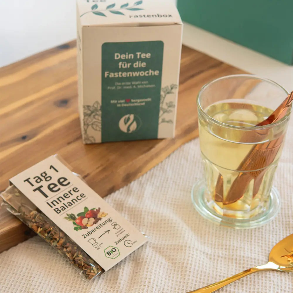 Glas Kräutertee neben einer Packung Fastentee