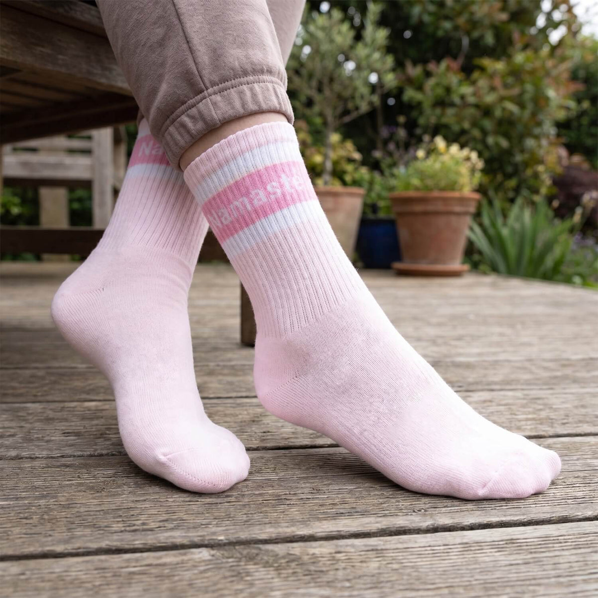 Rosa Namasté-Socken an den Füßen auf einer Holzterrasse