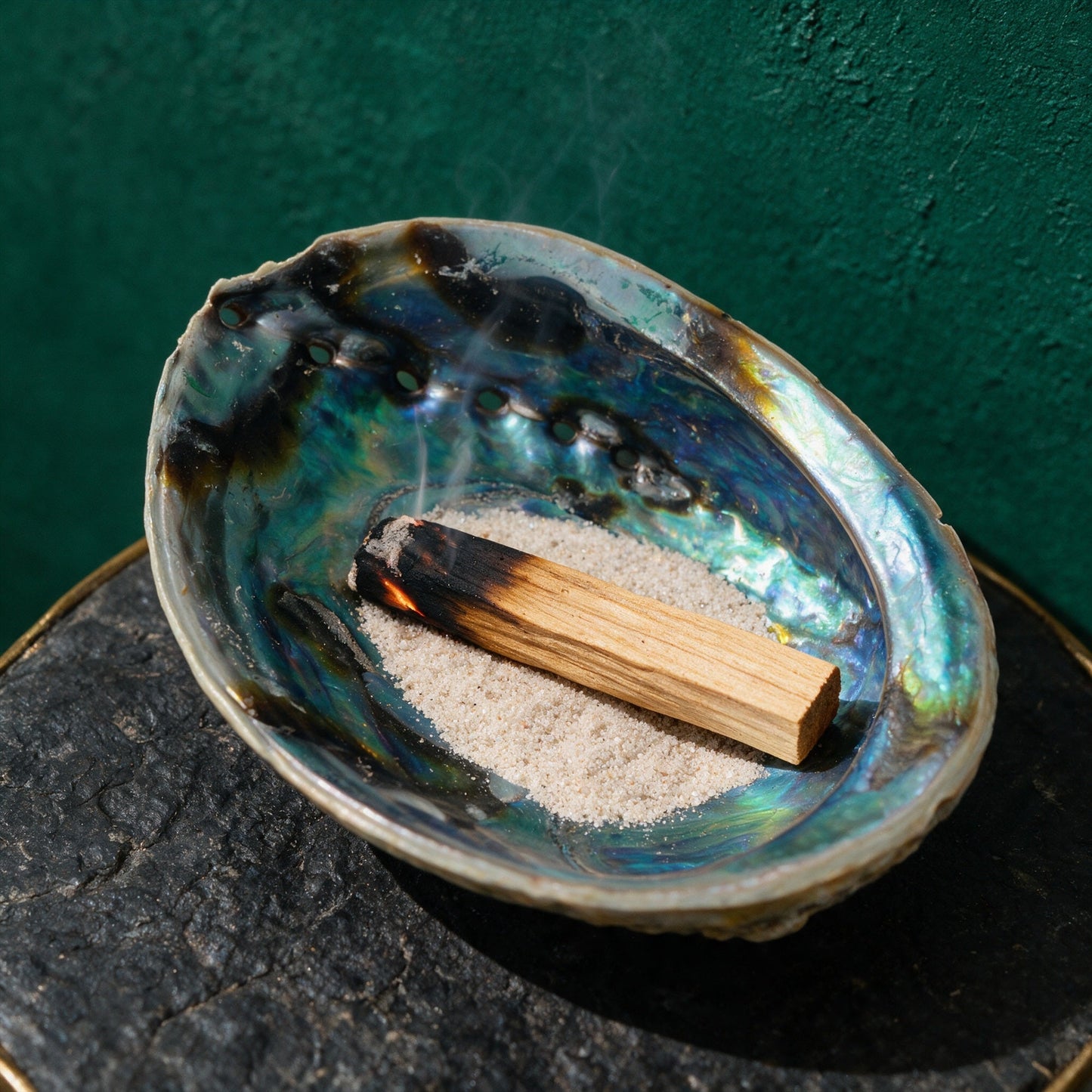 Regenbogen-Abalone-Paua-Muschel mit Sand und glimmendem Palo Santo als Räucherschale
