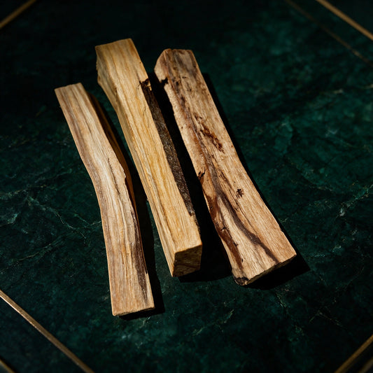 Drei Palo-Santo-Sticks von AURA AMARE vor tiefem Smaragdgrün