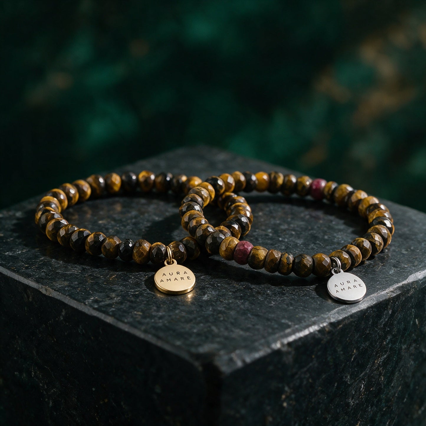 Tigerauge Armband in Gold und Silber von AURA AMARE vor tiefem Smaragdgrün