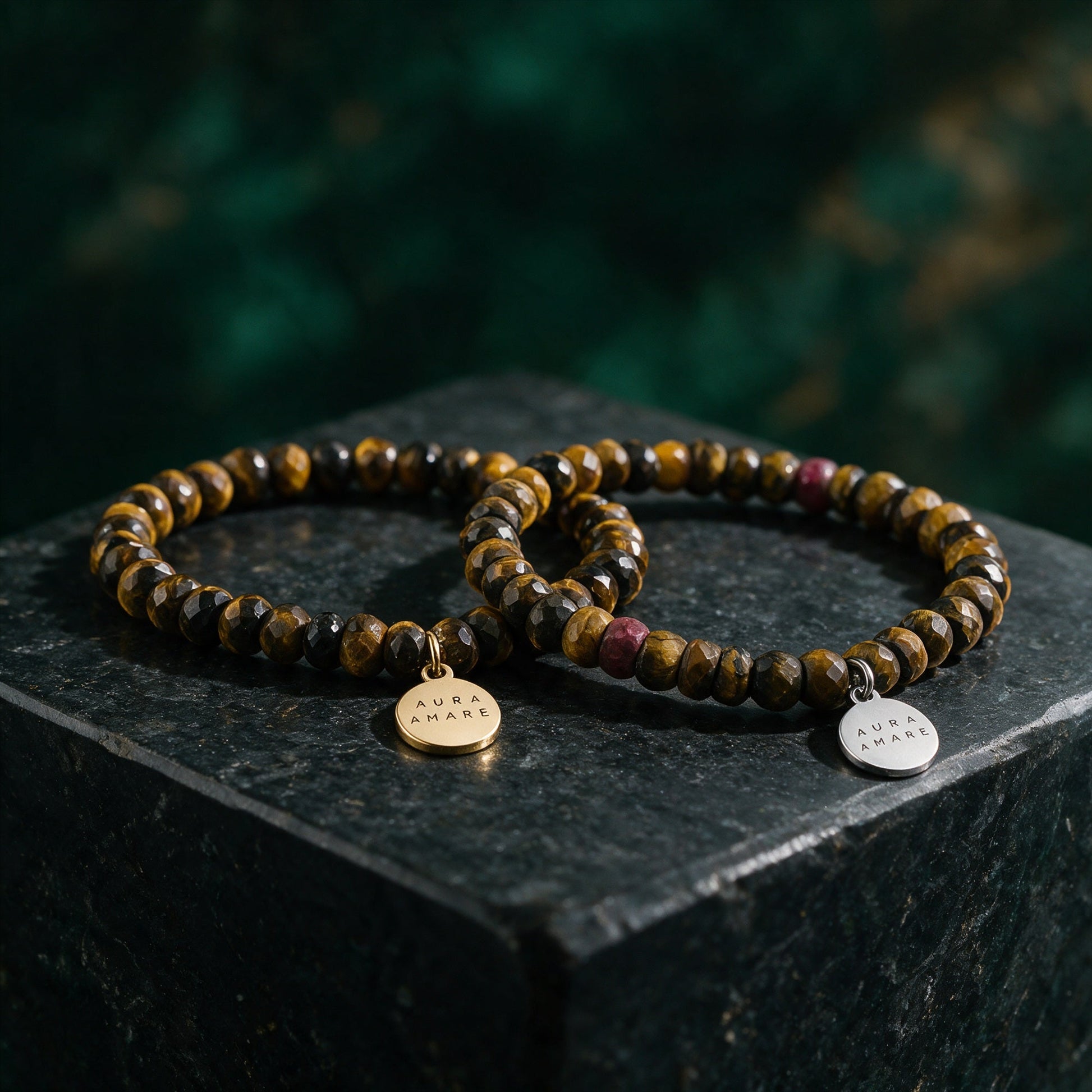 Tigerauge Armband in Gold und Silber von AURA AMARE vor tiefem Smaragdgrün