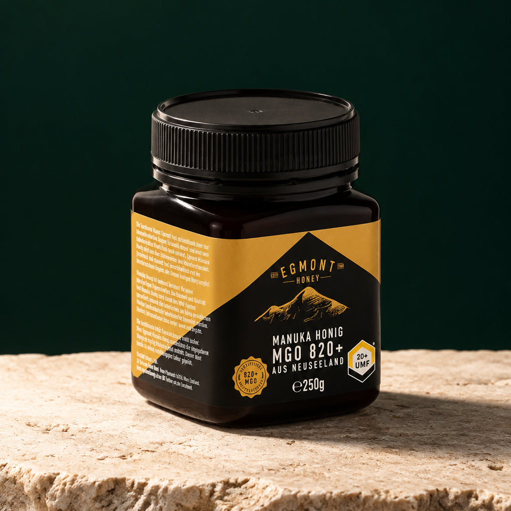 Glas Egmont Honey Manuka Honig MGO 820+ 250 g auf hellem Stein vor dunkelgrünem Hintergrund
