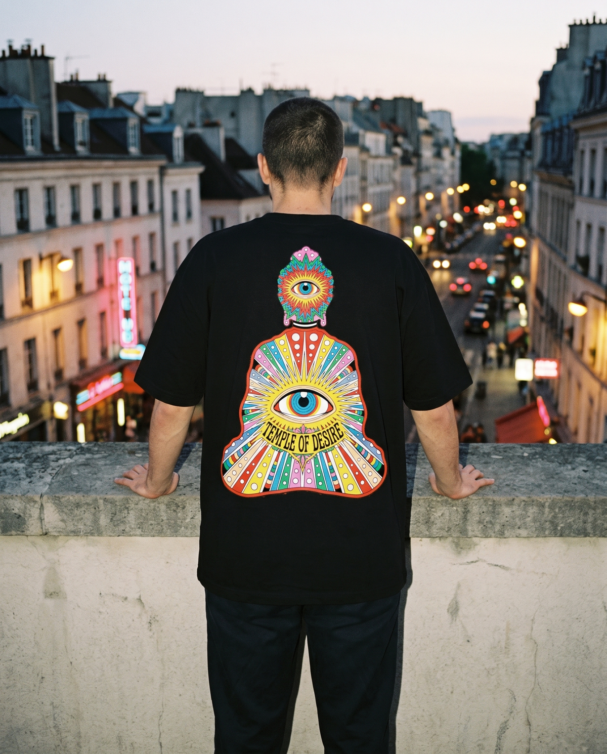 Der Sitzende — Strahlen: schwarzes Oversized-T-Shirt mit Rückenprint, getragen.