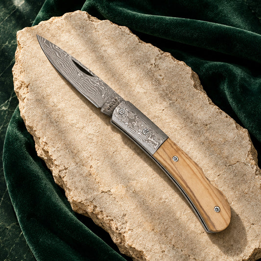Damast-Taschenmesser mit Olivenholzgriff und Damastbacken auf hellem Stein