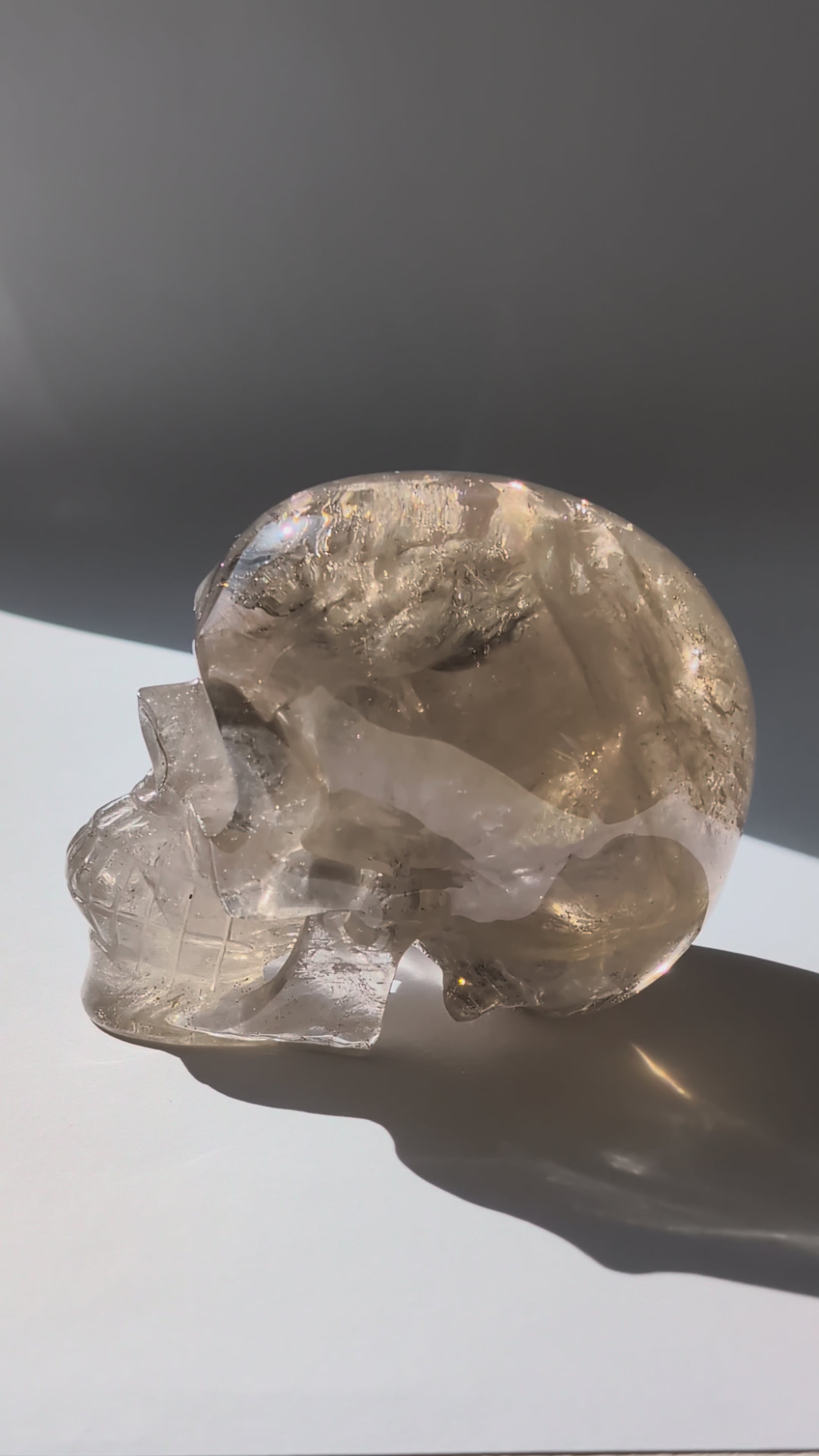 Ein 594g schwerer, klarer Rauchquarz-Schädel 'Der Wächter der Schatten' mit leuchtenden Regenbogen-Einschlüssen.