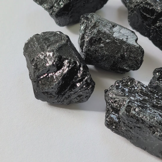 Eine Gruppe von rohen, tiefschwarzen Turmalin-Brocken (Schörl) mit glasartigem Glanz auf einer weißen Oberfläche.
