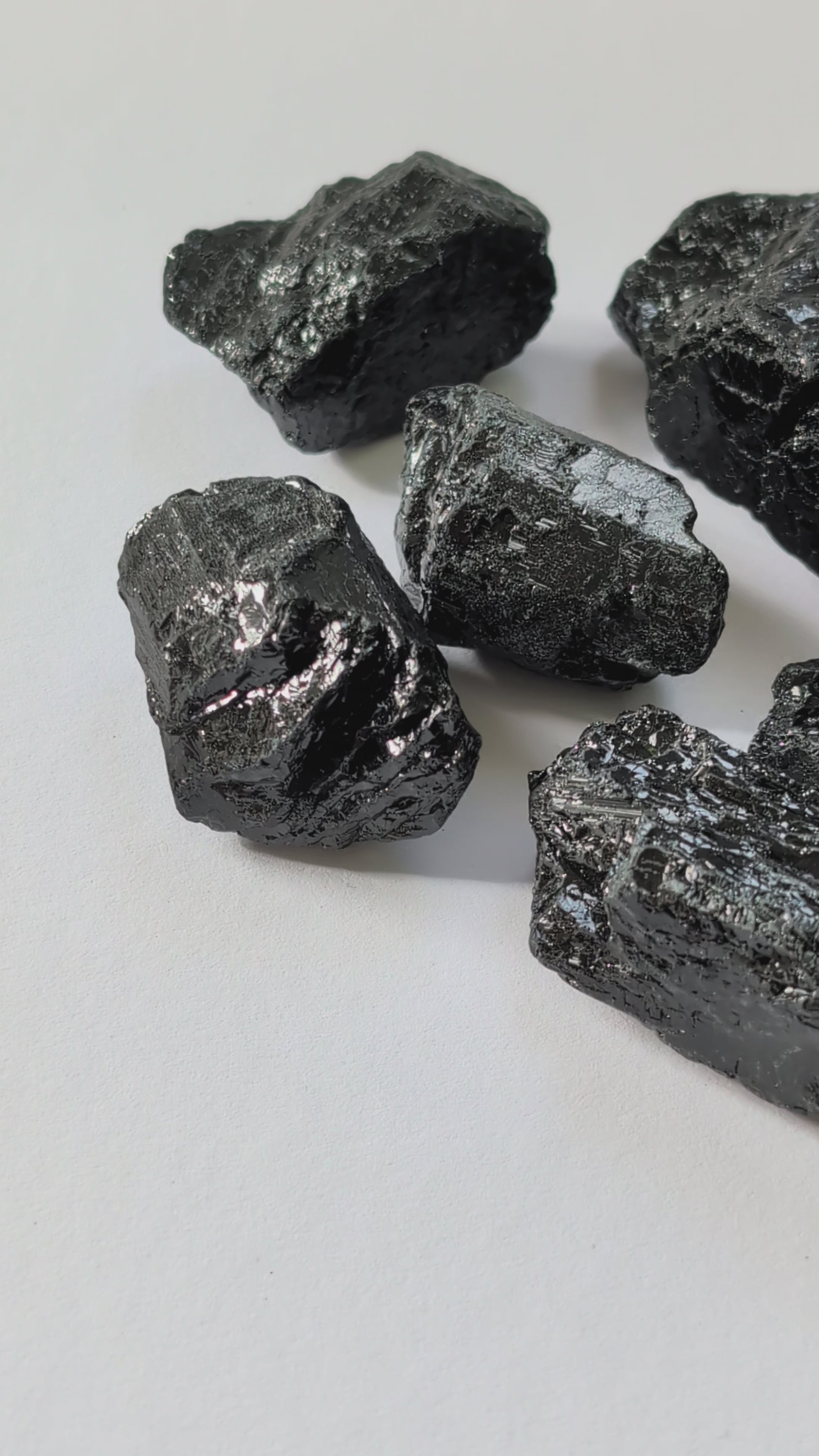 Eine Gruppe von rohen, tiefschwarzen Turmalin-Brocken (Schörl) mit glasartigem Glanz auf einer weißen Oberfläche.