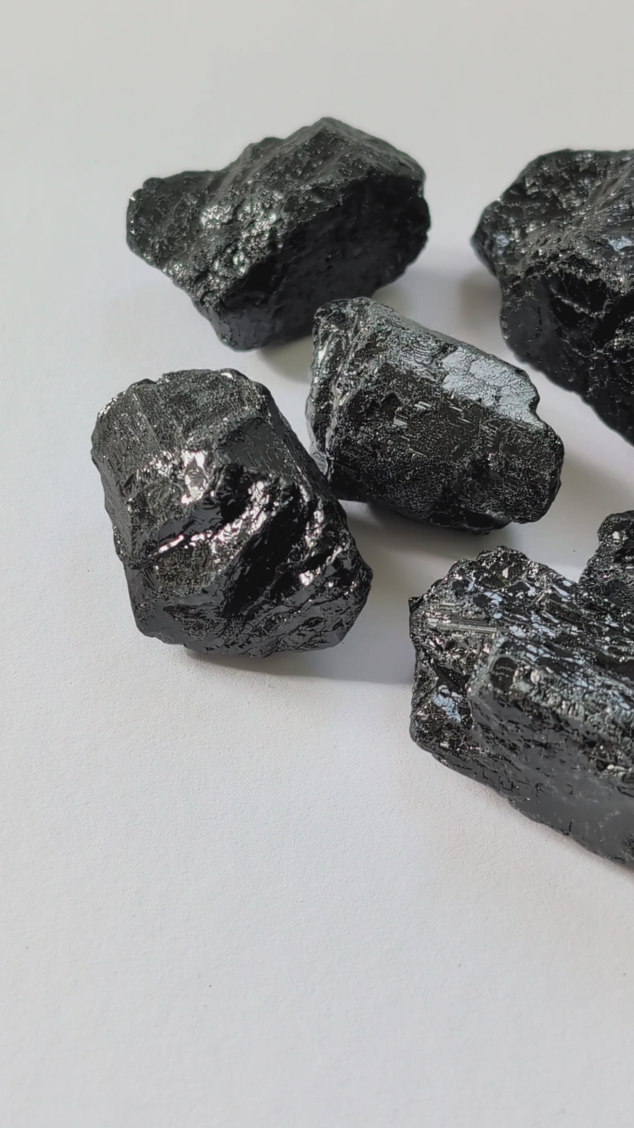 Eine Gruppe von rohen, tiefschwarzen Turmalin-Brocken (Schörl) mit glasartigem Glanz auf einer weißen Oberfläche.