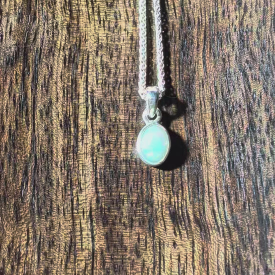 Polierter ovaler Opal Anhänger mit leuchtendem Farbspiel in einer schlichten 925er Silberfassung an einer Silberkette, energetisch aufgeladen von Temple of Desire