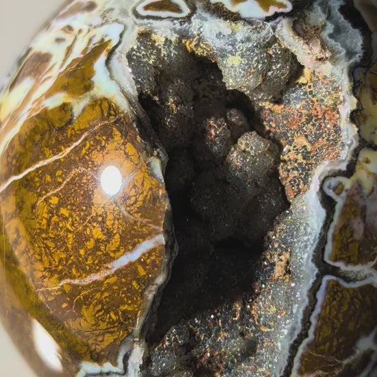 Polierte Drusenachat Kugel in Nahaufnahme mit offener Kristall-Geode und goldgelber Bänderung